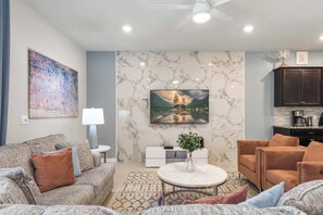 A modern living room with a sofa, armchairs, a coffee table, and a TV mounted on a marble wall. - Themed family retreat with epic game room (Davenport)