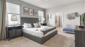 Une chambre à coucher avec un grand lit, des tables de chevet, un ventilateur de plafond et des œuvres d’art accrochées aux murs.