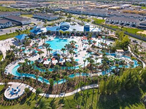 An aerial view of a resort with multiple swimming pools, palm trees, and a central building with a blue roof.