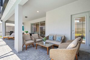 An outdoor patio with wicker furniture, a glass table, and a view through a glass door. - Themed family retreat with epic game room (Davenport)