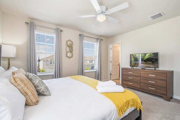 A bedroom with a bed, a dresser, a ceiling fan, and a television.
