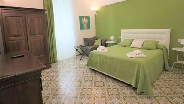 A bedroom with a green wall, a bed with green bedding, a wooden wardrobe, and a green curtain.