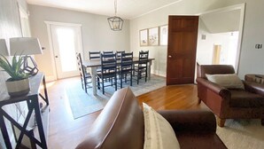A spacious living room with a brown leather sofa, a dining table with chairs, and a wooden door. - Dwntwn Custer Farmhouse on Main St. with Hot Tub (Custer)