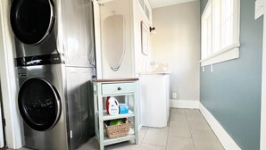 A laundry room with two stacked front-loading washers and dryers, a small white cabinet, and a basket with laundry supplies. - Dwntwn Custer Farmhouse on Main St. with Hot Tub (Custer)