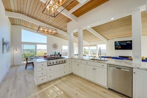 A spacious kitchen with a large island, wooden ceiling beams, and a view of the outdoors.