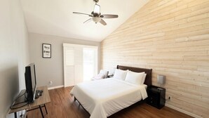 A bedroom with a bed, a desk with a computer, a ceiling fan, and a wooden wall. - Paradise Home in Discovery Bay minutes to fast water (Discovery Bay)