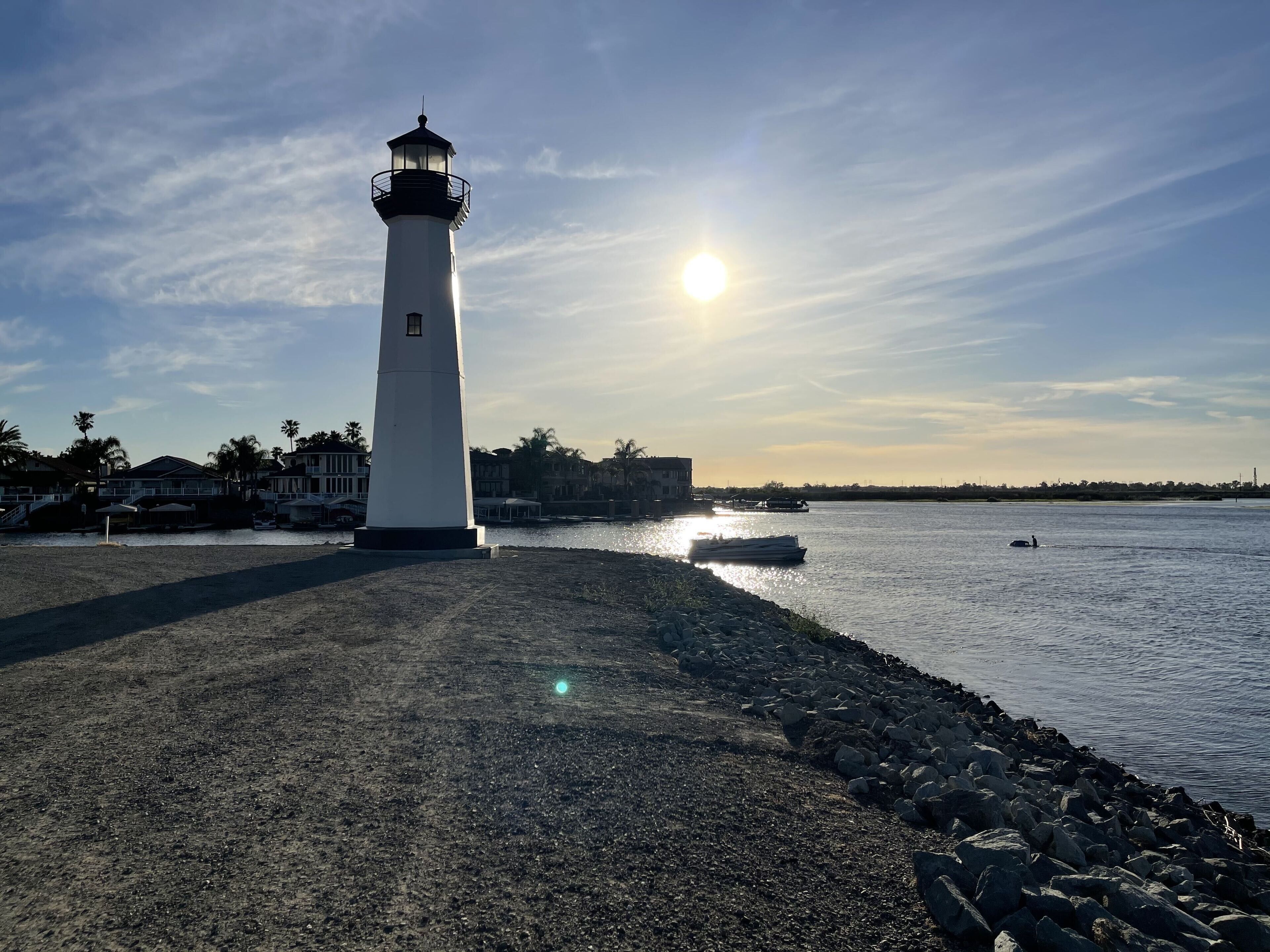 A lighthouse by a rocky shore with a clear sky and calm water.