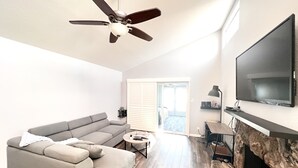 A modern living room with a gray sectional sofa, a ceiling fan, a flat-screen TV mounted on the wall, and a fireplace. - Paradise Home in Discovery Bay minutes to fast water (Discovery Bay)