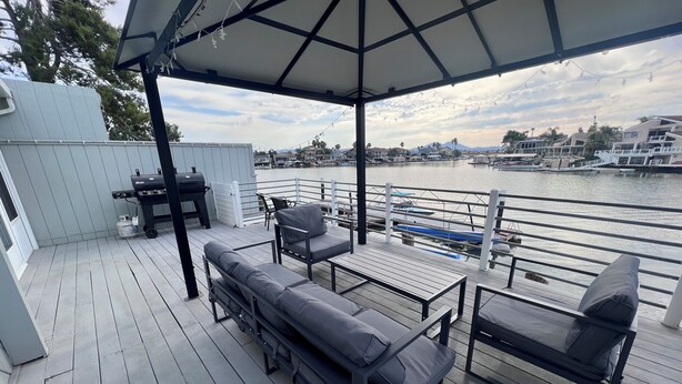 A covered deck with outdoor furniture, a grill, and a view of a marina with boats. - Paradise Home in Discovery Bay minutes to fast water (Discovery Bay)