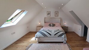 Un dormitorio con techo inclinado, tragaluces, cama con colcha estampada, mesitas de noche con lámparas y una alfombra pequeña.