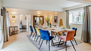 A dining area with a long table set for six, surrounded by colorful chairs, a window with curtains, and a hallway leading to another room. - Court Lodge is a substantial and picturesque twin roundel oast house set in pretty gardens within th (Heathfield)