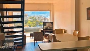 A modern living room with a dining area, large windows, and a view of buildings and trees. - Duerme Ushuaia (Ushuaia)