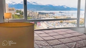 A bedroom with a large window offering a view of a cityscape and mountains. - Duerme Ushuaia (Ushuaia)