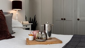 Un lit bien fait, sur lequel repose un plateau en bois contenant une cafetière, des tasses et une théière.