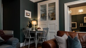 Una sala de estar con un sofá de cuero marrón, un sillón gris y una mesa de comedor con sillas. Hay un aparador blanco con puertas de cristal contra la pared.