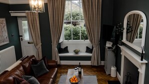 Un salón acogedor con un sofá de cuero marrón, una mesa de centro de madera con un cuenco de naranjas, una chimenea y una ventana con cortinas.