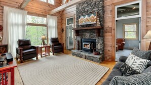 A cozy living room with a stone fireplace, wooden beams, and a large window. - Enjoy cookouts on the deck and peaceful valley views! - Elemental Bliss (Jasper)