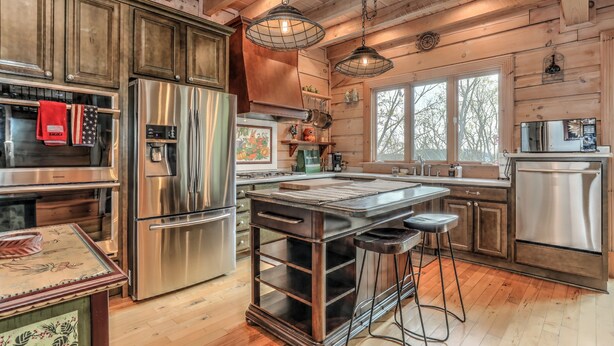 A spacious kitchen with wooden walls, stainless steel appliances, and a large island with stools. - Enjoy cookouts on the deck and peaceful valley views! - Elemental Bliss (Jasper)