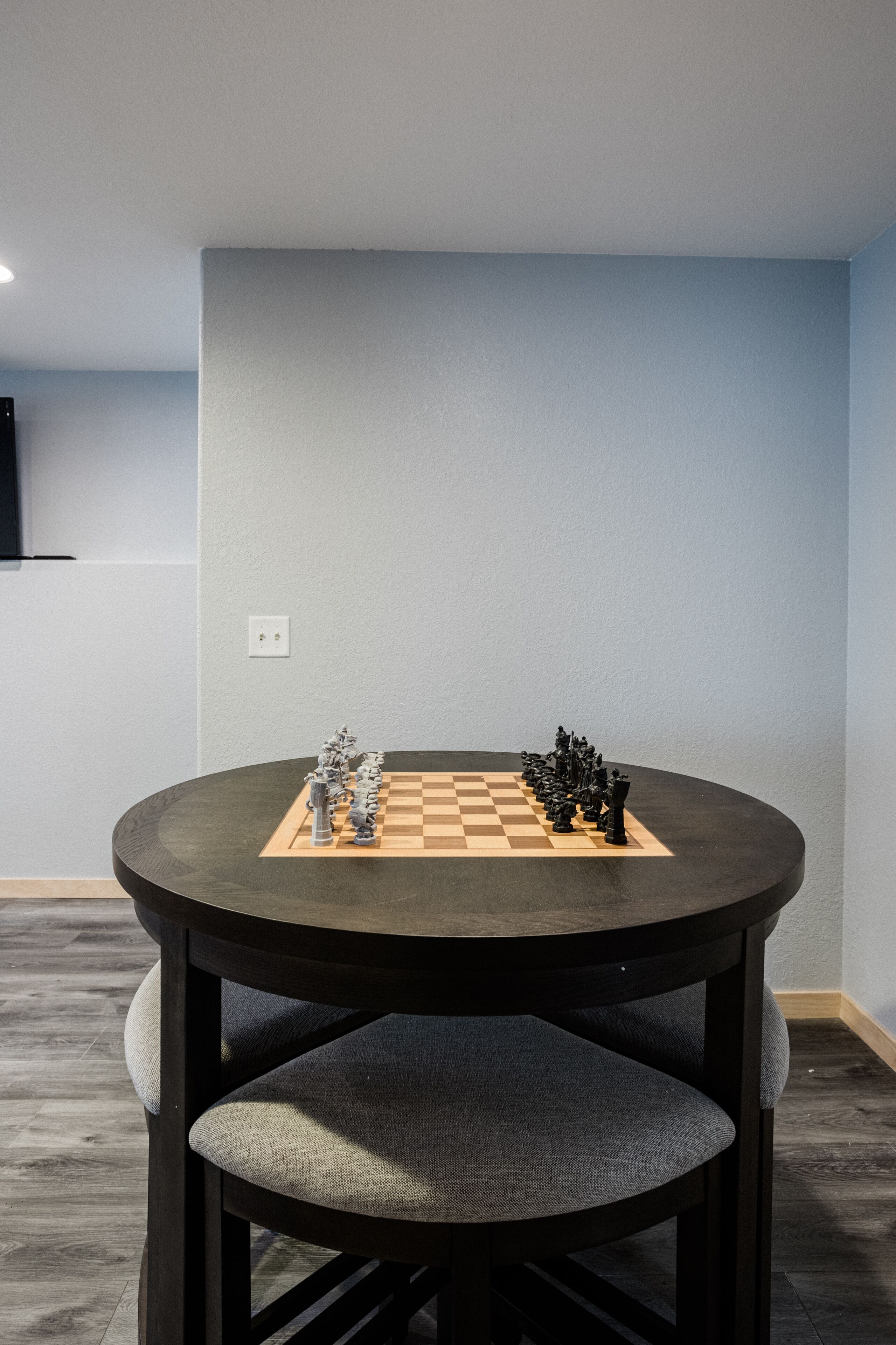 A round table with a chessboard, two chairs, and a wall-mounted TV.