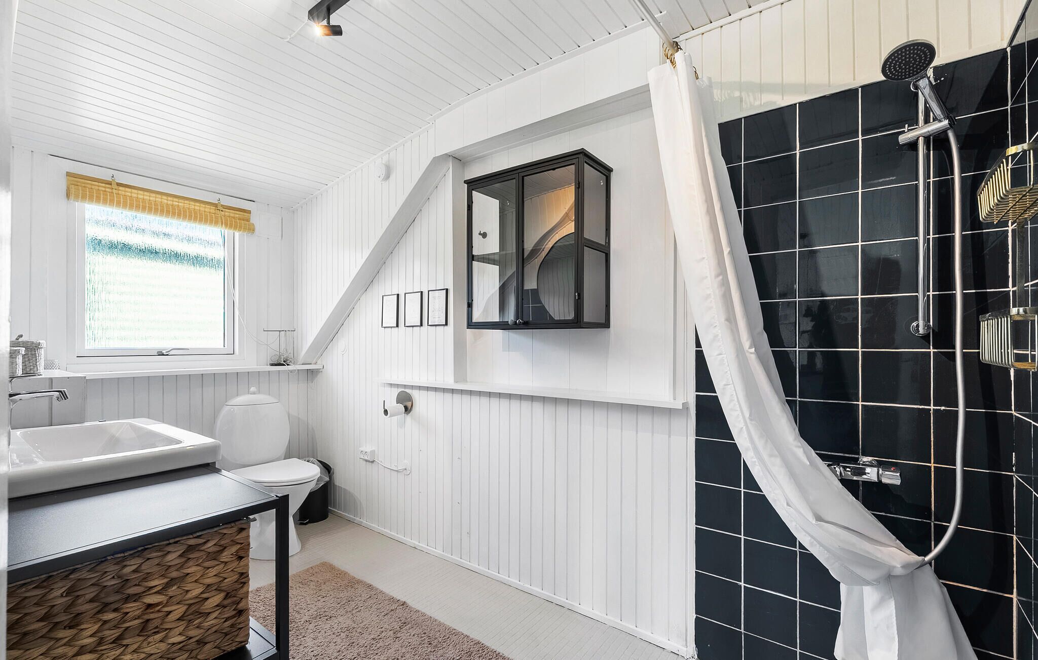 A bathroom with a white sink, toilet, and shower area with black tiles.