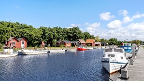 A marina with several boats docked, a wooden pier, and red buildings in the background.