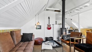 A cozy loft-style living room with a high ceiling, a fireplace, a sofa, a coffee table, and a guitar.