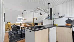 A modern kitchen with a central island, black countertops, and a built-in dishwasher.