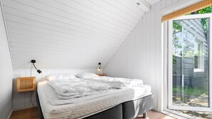 A bedroom with a sloped ceiling, a bed with white bedding, a bedside lamp, and a window with a view of greenery.