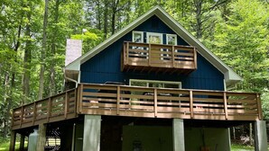 A cabin with a wooden deck and a second-story balcony, surrounded by trees.