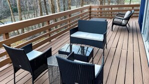 A wooden deck with wicker furniture, including chairs and a table, overlooking a forested area.