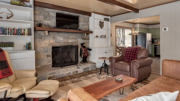 A cozy living room with a stone fireplace, leather sofas, a wooden coffee table, and a bookshelf filled with books.