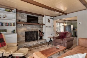 A cozy living room with a stone fireplace, leather sofas, a wooden coffee table, and a bookshelf filled with books.