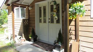 Una casa di legno con una porta bianca, un piccolo portico e un cesto di fiori appeso.