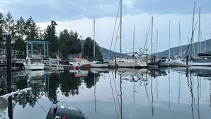Una marina con diverse barche a vela ormeggiate, una piccola imbarcazione con motore fuoribordo Suzuki e un edificio con tetto blu sullo sfondo.