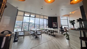 A modern dining area with large windows offering a city view, wooden flooring, and pendant lighting.