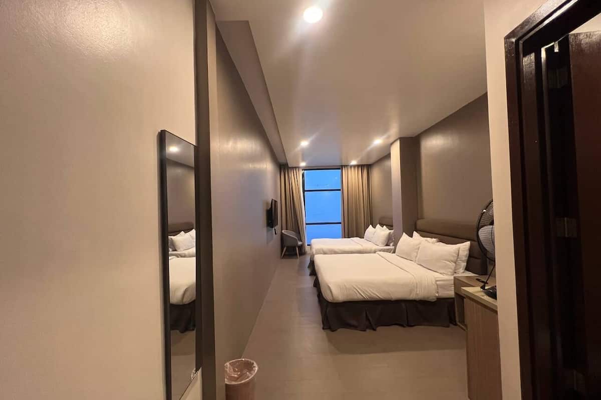 Habitación de hotel con dos camas, un escritorio, una silla, un televisor y un ventanal con cortinas.