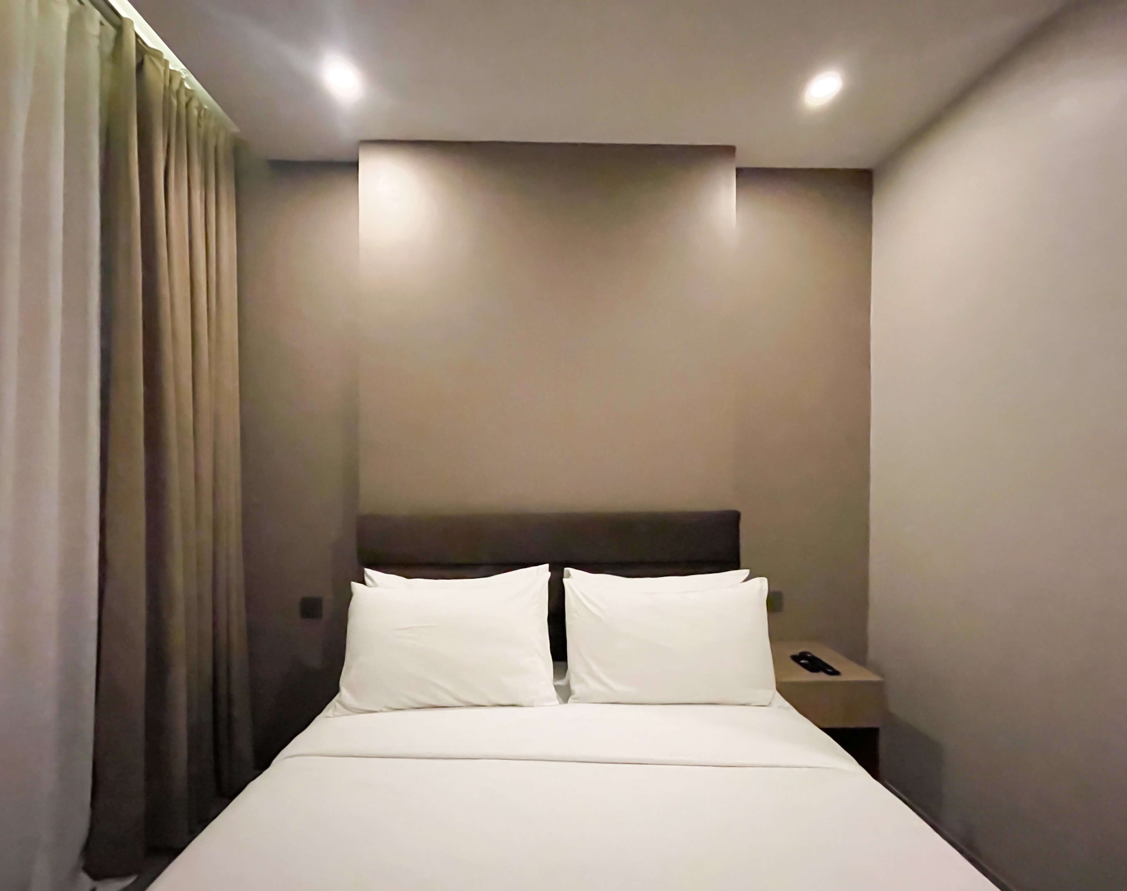 Habitación de hotel con una cama, dos almohadas, una mesita de noche, un teléfono y una cortina.