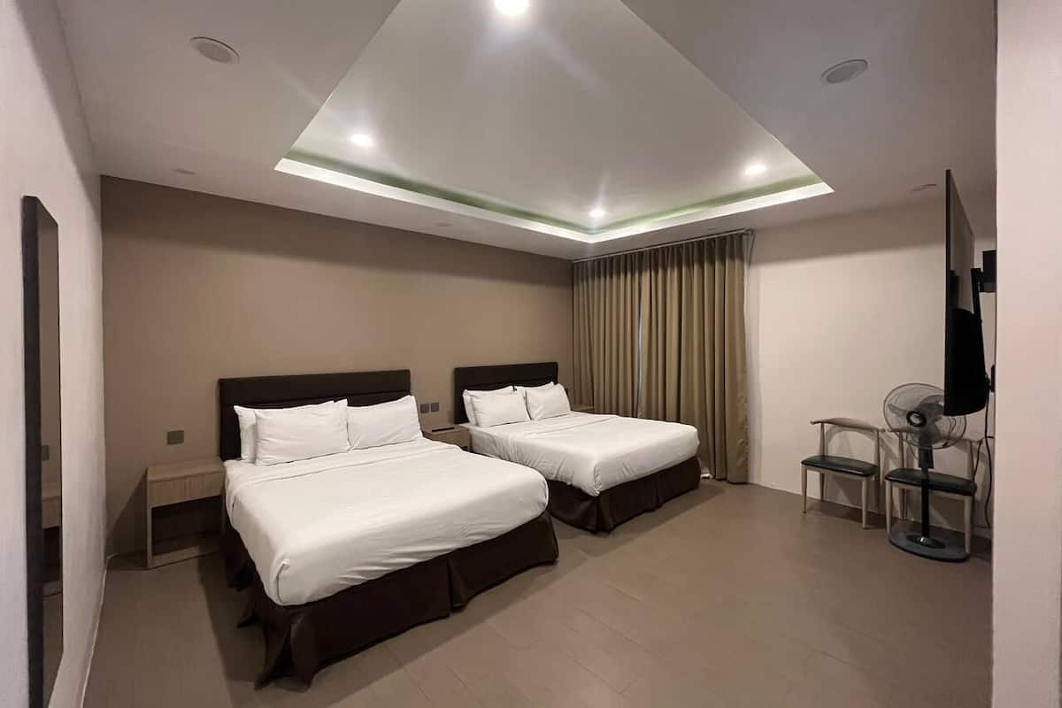 Una habitación de hotel con dos camas, una lámpara en el techo, un televisor y un ventilador.
