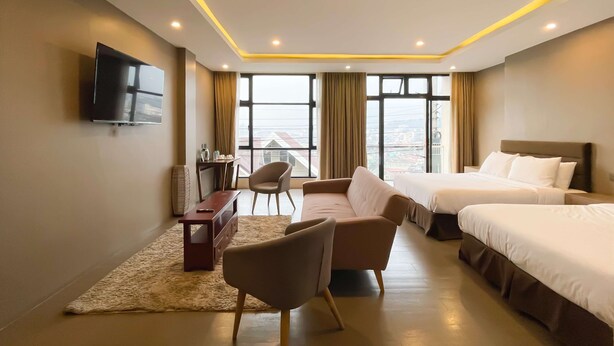 A hotel room with two beds, a desk, a chair, and a TV.