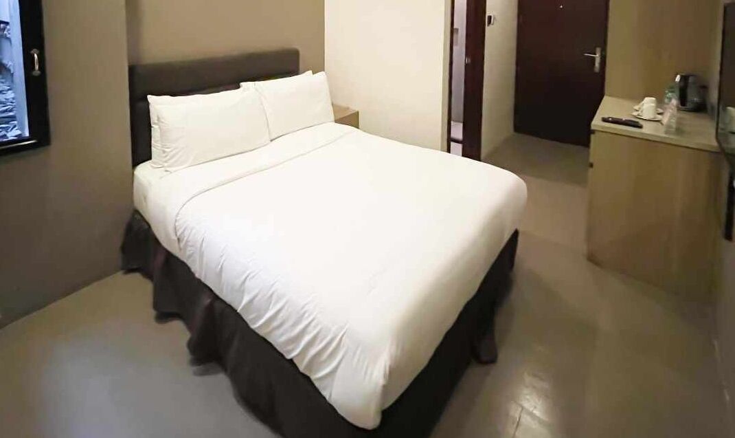 A neatly made bed with white linens in a hotel room.