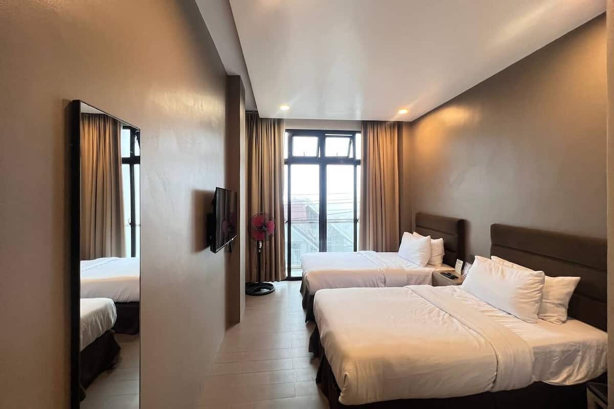 Habitación de hotel con dos camas, un televisor de pantalla plana, un ventilador y un amplio ventanal con cortinas.