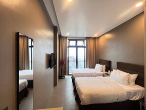 Habitación de hotel con dos camas, un televisor de pantalla plana, un ventilador y un amplio ventanal con cortinas.