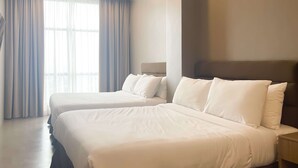 A hotel room with two beds, a large window with curtains, a modern ceiling light, and a plain wall.
