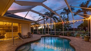 A swimming pool with string lights, a covered patio, and chairs. - Solar Heated Pool, Hot Tub, Kayaks, Canal Views - Villa Tranquil Haven- Roelens Vacations (Cape Coral)