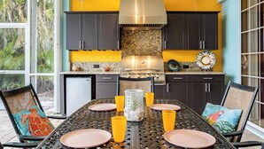 A kitchen with a yellow wall, dark cabinets, and a stainless steel range hood. There is a dining table with chairs and orange cups. - Solar Heated Pool, Hot Tub, Kayaks, Canal Views - Villa Tranquil Haven- Roelens Vacations (Cape Coral)