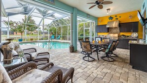 A spacious patio area with a pool, outdoor dining set, and a kitchen with a yellow accent wall. - Solar Heated Pool, Hot Tub, Kayaks, Canal Views - Villa Tranquil Haven- Roelens Vacations (Cape Coral)