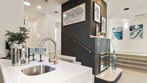 A modern kitchen with a marble countertop, stainless steel sink, and a black accent wall with artwork.