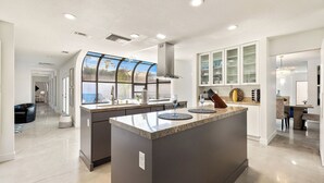 Una cocina moderna con una isla central, electrodomésticos integrados y un amplio ventanal con vistas a un jardín trasero.