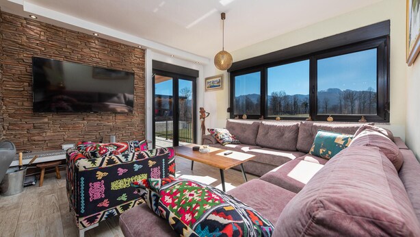 A modern living room with a stone wall, a large flat-screen TV, a sofa set, and a view of mountains through large windows. - Lovely home in Ornice (Ornice)