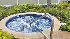 A hot tub with a metal ladder, surrounded by greenery and a white fence.